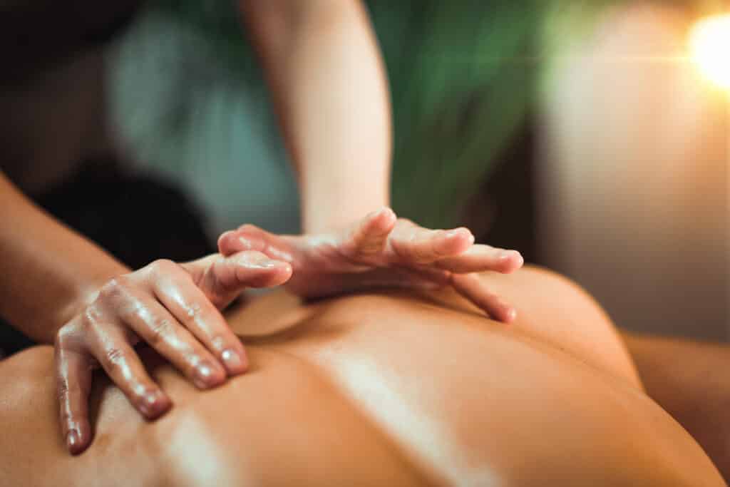 Mains huileuses massant le dos d'une personne, ambiance relaxante avec lumière douce.